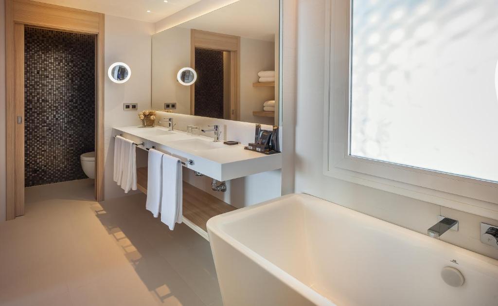 Mūsdienīgas vannas istabas interjers ar diviem izlietnēm, vannu un elegantiem apgaismojuma risinājumiem. Tumšas mozaīkas sienas piešķir telpai stilīgu izskatu.