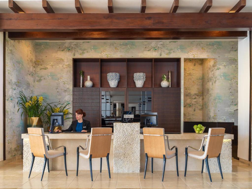 Mūsdienīgs viesnīcas reģistratūras interjers ar koka griestiem un dabīgiem elementiem, kurā strādā darbiniece. Stilīga apdare un augi piešķir siltumu un viesmīlību.