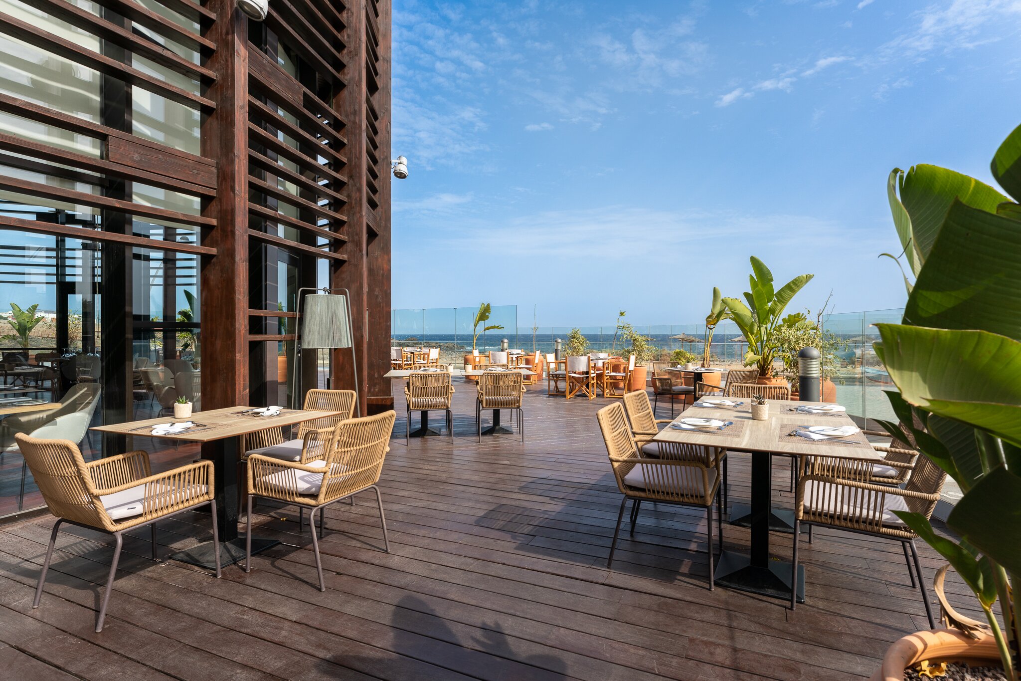 Labi iekārtota terase ar modernām mēbelēm un skatu uz jūru, radot patīkamu atmosfēru ēdināšanai. Terase ir apzaļumota ar augiem, piedāvājot relaksējošu vidi.