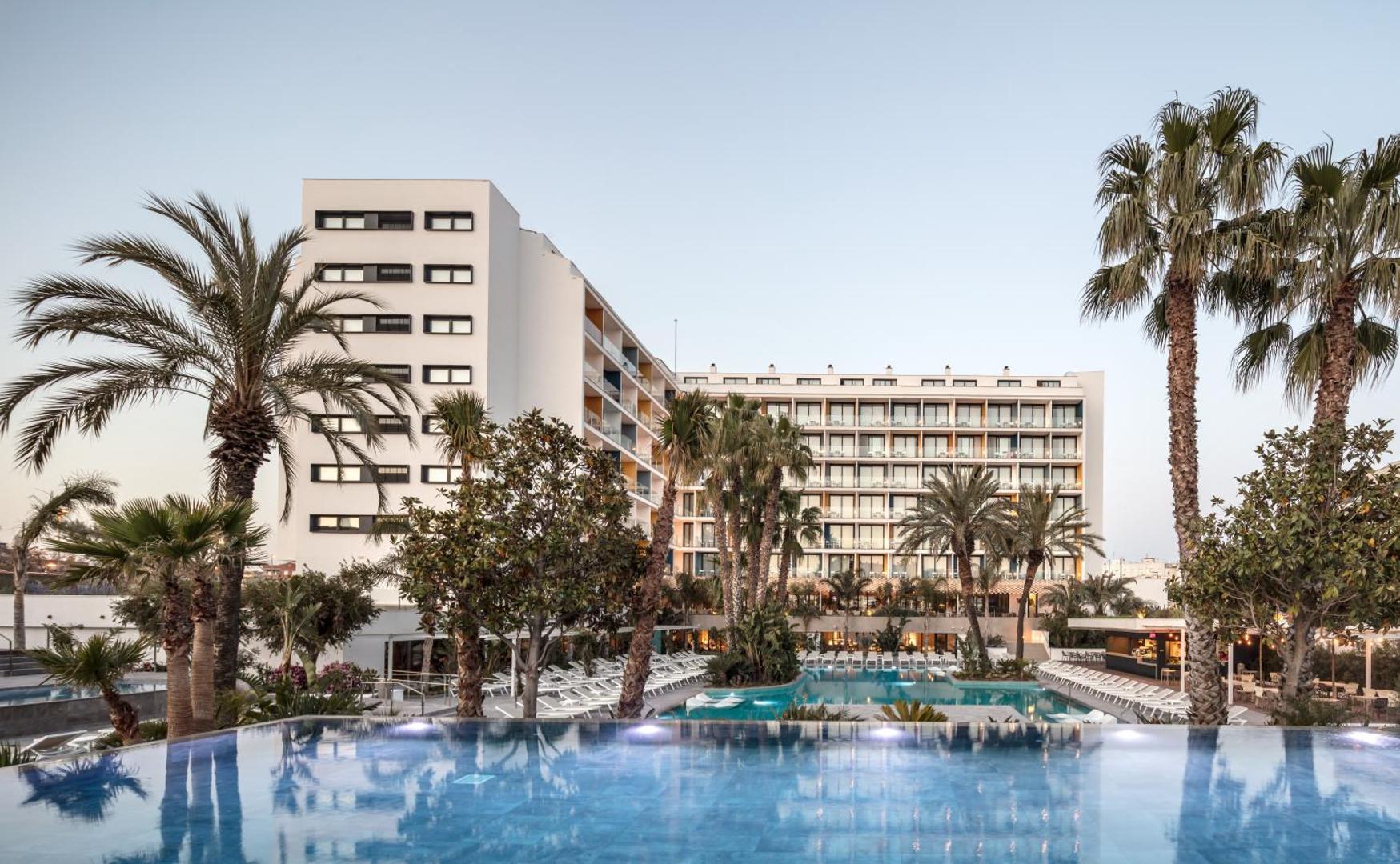AQUA Hotel Silhouette & Spa ēkas fasāde vakarā ar izgaismotu āra baseinu, atpūtas krēsliem un palmām Malgrat de Mar kūrortā.
