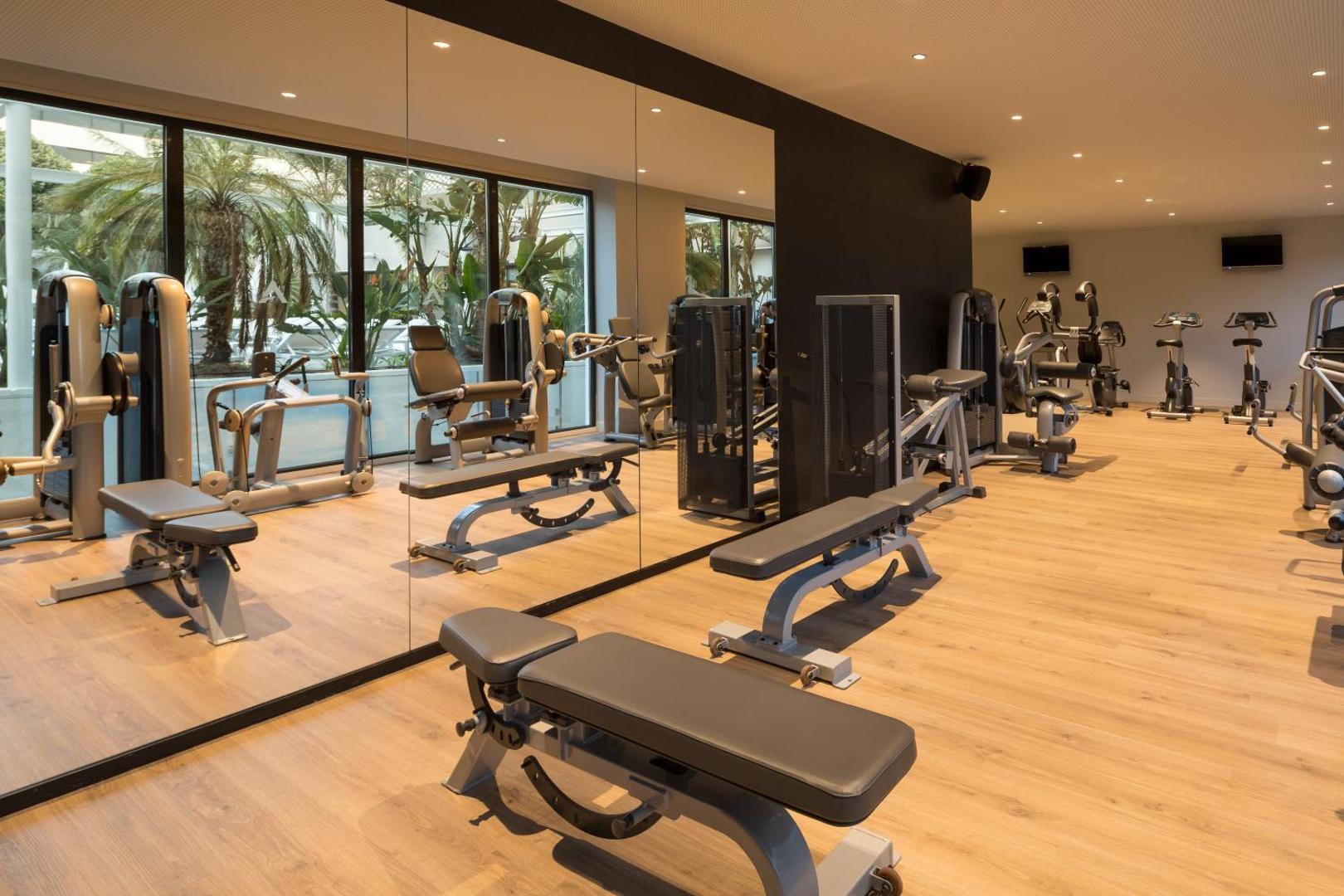 Mūsdienīgs AQUA Hotel Silhouette & Spa fitness centrs ar trenažieriem, spoguļsienu un skatu uz dārzu caur lielajiem logiem.