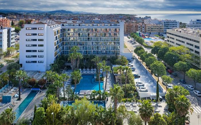 AQUA Hotel Silhouette & Spa teritorijas skats no augšas ar baseiniem, palmām un pilsētas panorāmu piekrastē