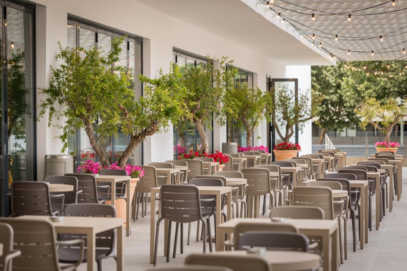 AQUA Hotel Silhouette & Spa āra terase ar galdiņiem un krēsliem, ko ieskauj dekoratīvi koki podos un ziedi Malgrat de Mar kūrortā
