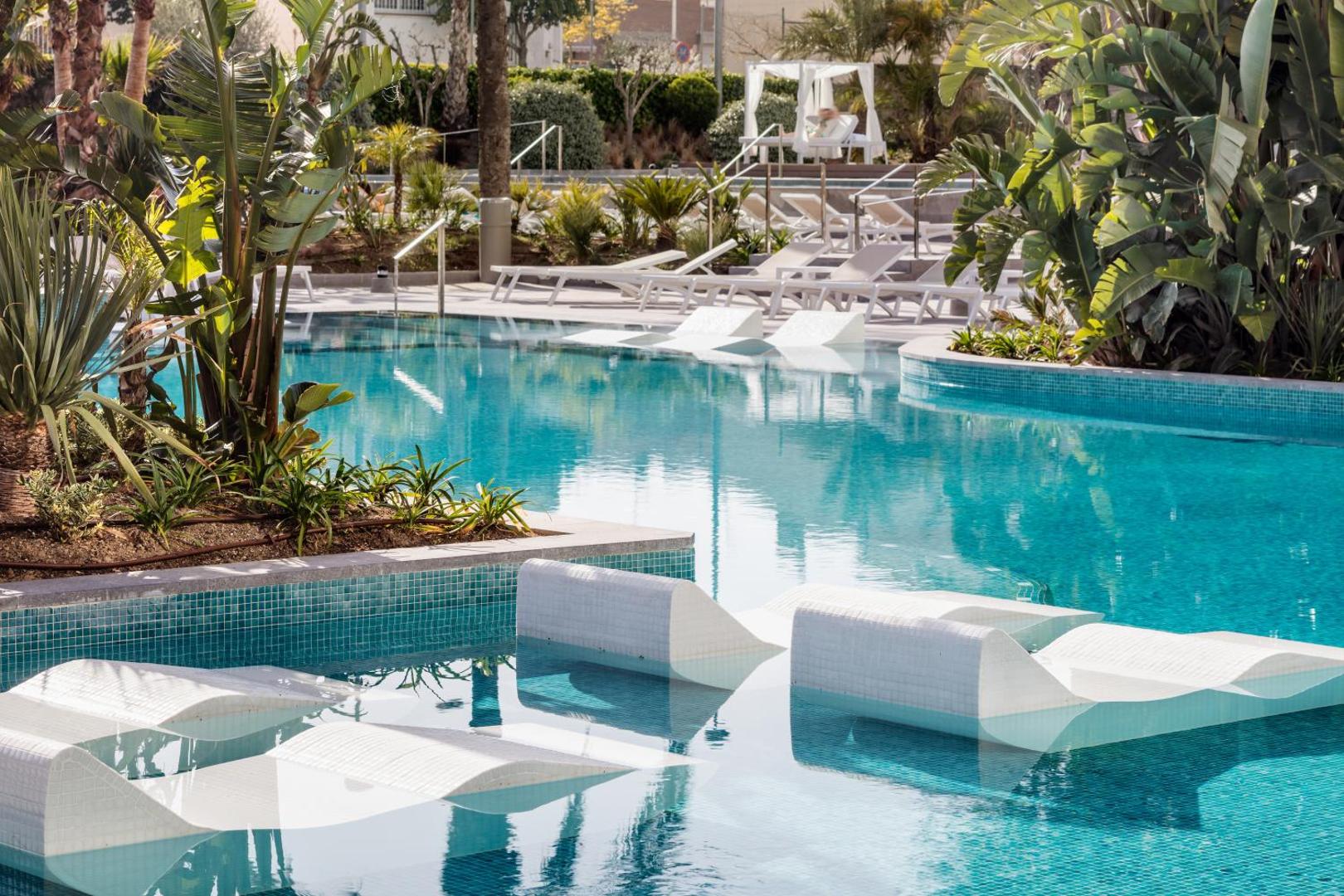Tuvplāns AQUA Hotel Silhouette & Spa baseinam ar ergonomiskiem sauļošanās krēsliem ūdenī un tropiskiem augiem apkārtnē.