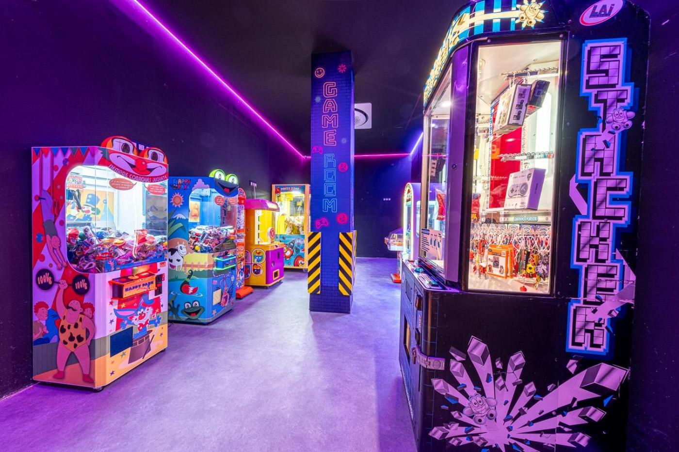 Estival Park Marena spēļu zāle ar neona gaismām un dažādiem spēļu automātiem, piedāvājot izklaides iespējas pusaudžiem un pieaugušajiem.