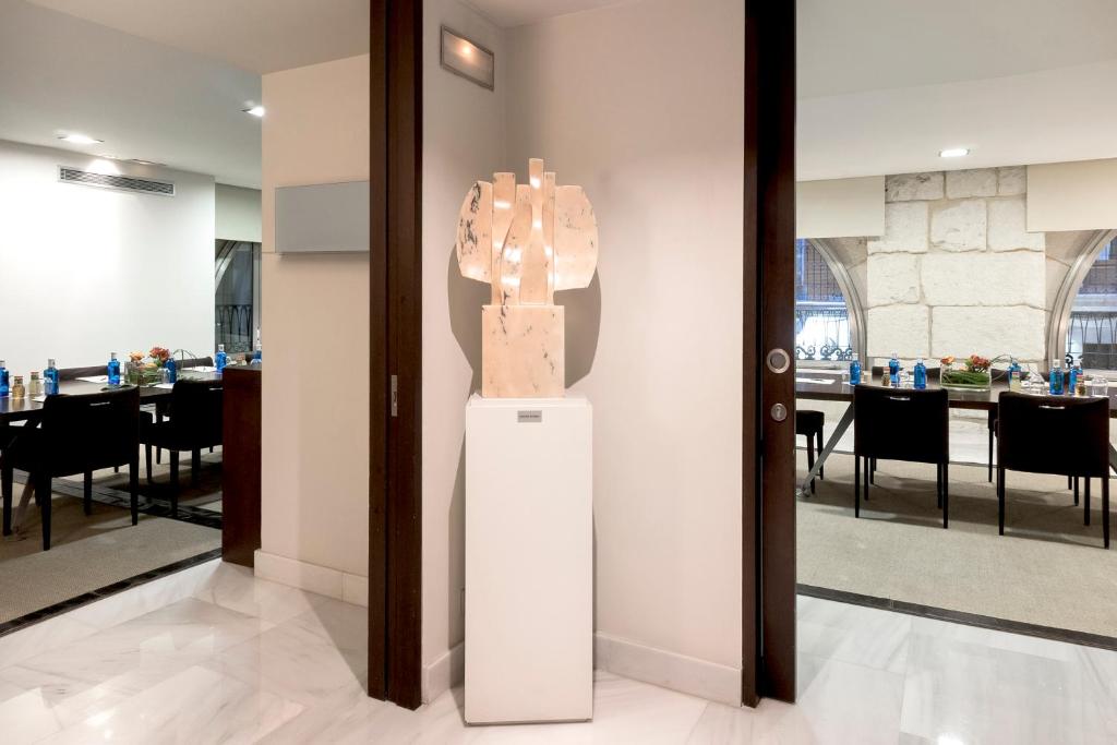 Mūsdienīga telpa ar dekoratīvu skulptūru, kas novietota pie durvīm, un izkārtotiem galdiem blakus. Gaismas un interjera elementi rada elegantu atmosfēru.