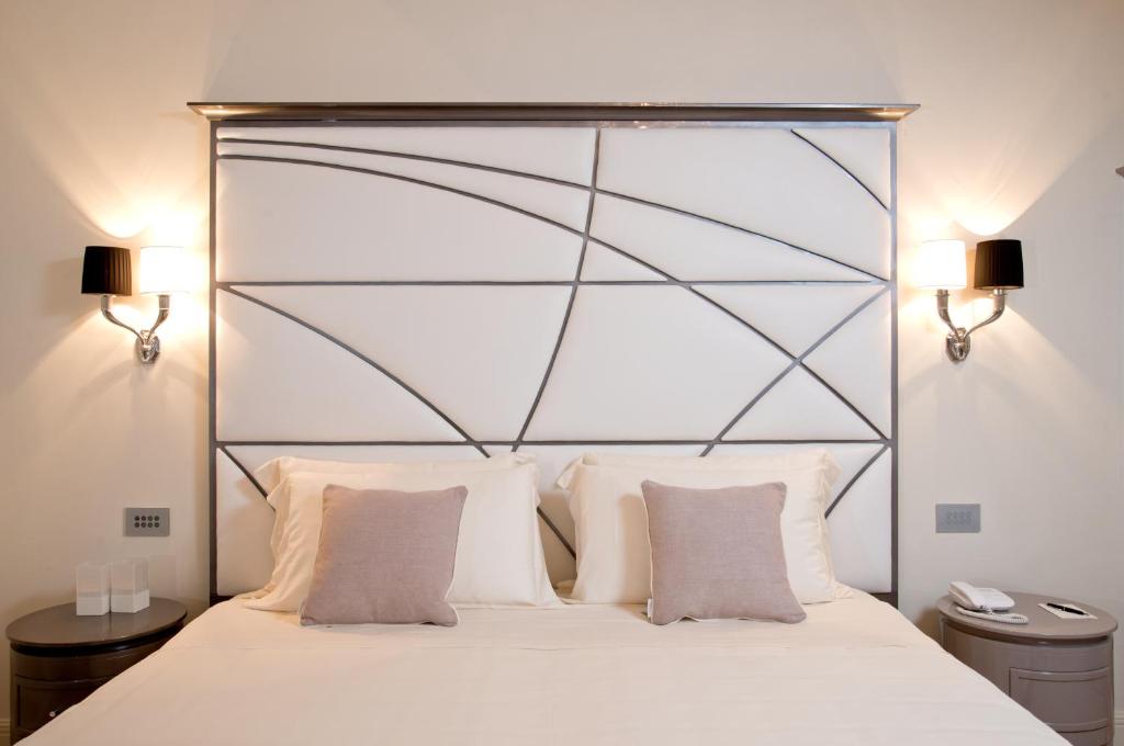 Mūsdienīgs guļamistabas interjers ar elegantām gultas veļām un stilīgu gultas galvu, kas papildināta ar sienas lampām abās pusēs.