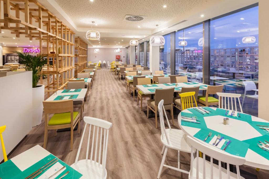 Mūsdienīgs restorāns ar gaišu interjeru un elegantiem galdiem, kas dekorēti ar zaļām galdautām. Logi nodrošina plašu skatu, radot patīkamu atmosfēru.