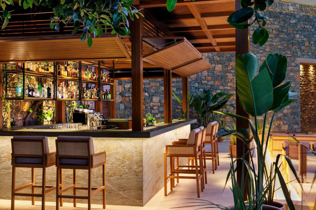 Daios Cove Luxury Resort bārs ar elegantiem krēsliem un dzērienu plauktiem.