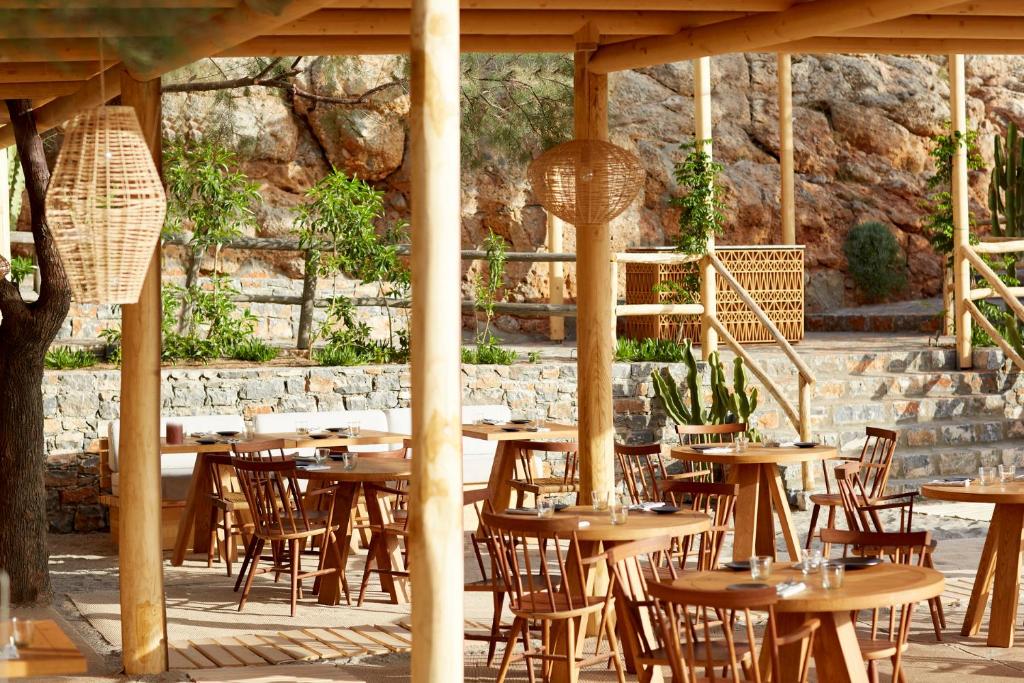 Daios Cove Luxury Resort āra restorāns ar koka galdiem un dabas elementiem.
