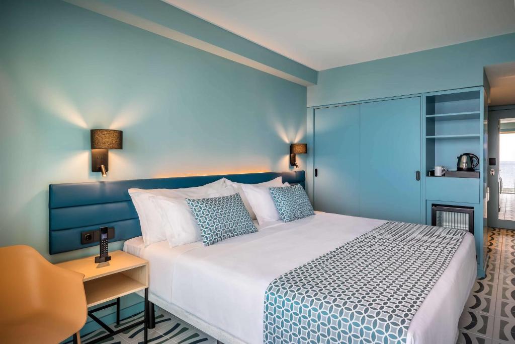 Mūsdienīga viesnīcas numura iekārtojums ar gaišām krāsām, divguļamo gultu un stilīgu mēbeļu kombināciju. Numurā ir iekārtota zona ar mini ledusskapi un elektrisko tējas vārītāju.