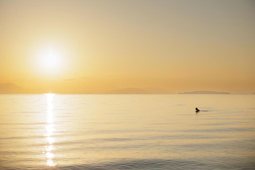 Saulriets pār mierīgu ūdeni, kurā peld cilvēks. Šī aina rada mierīgu un relaksējošu atmosfēru.