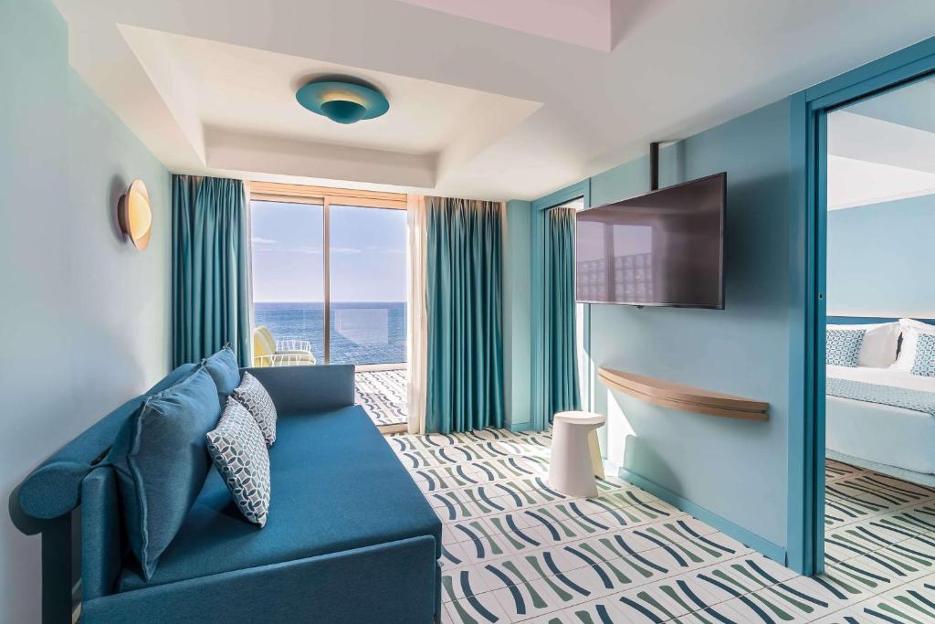 Moderna viesnīcas istaba ar jūras skatu, gaišām krāsām un stilīgu dizainu, kurā ir dīvāns, televizors un balkons.