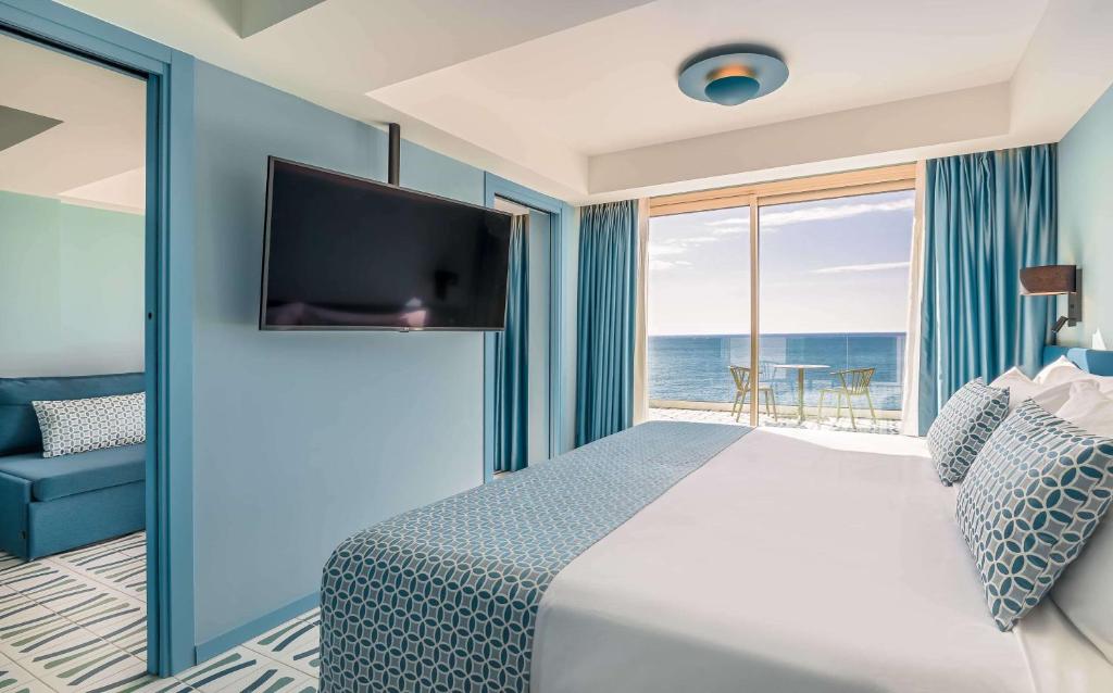 Mūsdienīgs viesnīcas numurs ar skatu uz jūru, iekārtots gaišos toņos ar zilu akcentu, kurā ir liels televizors un ērta dīvāna zona. Numurā ir pieejams balkons ar galdu un krēsliem, kas nodrošina relaksējošu atmosfēru.