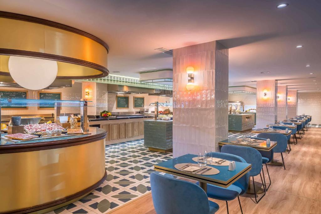 Mūsdienīgs restorāns ar elegantām mēbelēm un izsmalcinātu interjeru, kurā redzami ēdināšanas stendi un stilīgi galdi. Gaisotne ir silta un aicinoša, ideāla maltīšu baudīšanai.