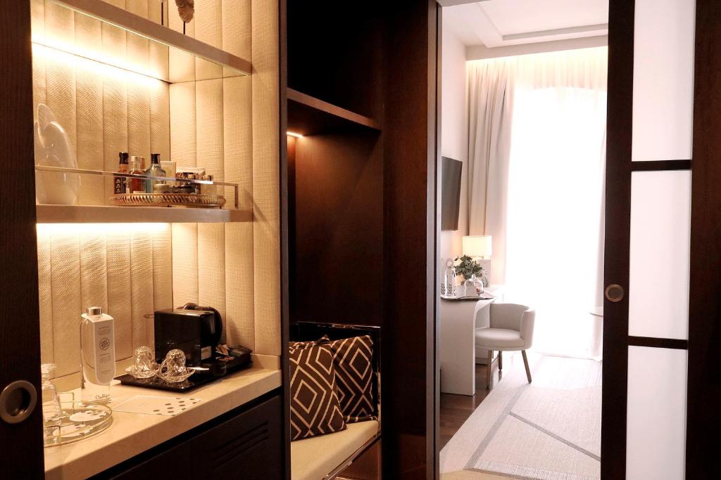 Elegants viesnīcas numura interjers ar mini bāru, tējkannu un komfortablu sēdvietu. Gaisma izgaismo telpu, radot mājīgu atmosfēru.