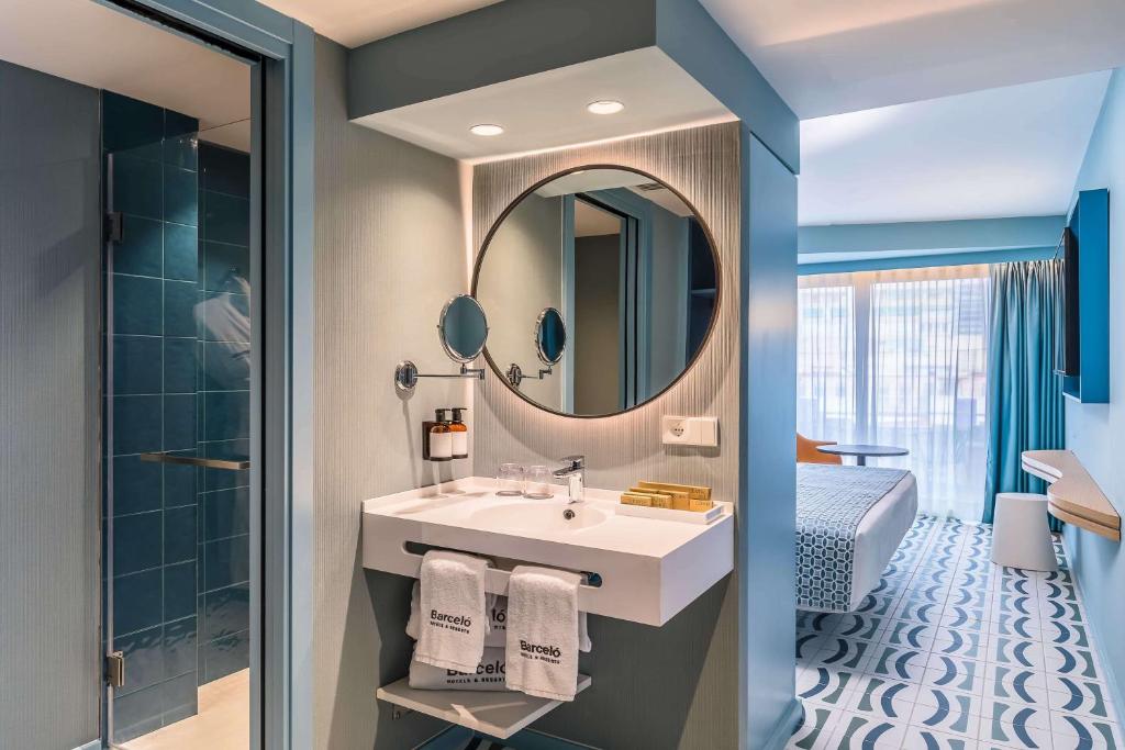 Mūsdienīgs viesnīcas numurs ar elegantu vannas istabu, kurā ir moderna izlietne un liels spogulis. Telpā ir gaiša krāsu shēma un mūsdienīgs dizains, kas rada patīkamu atmosfēru.