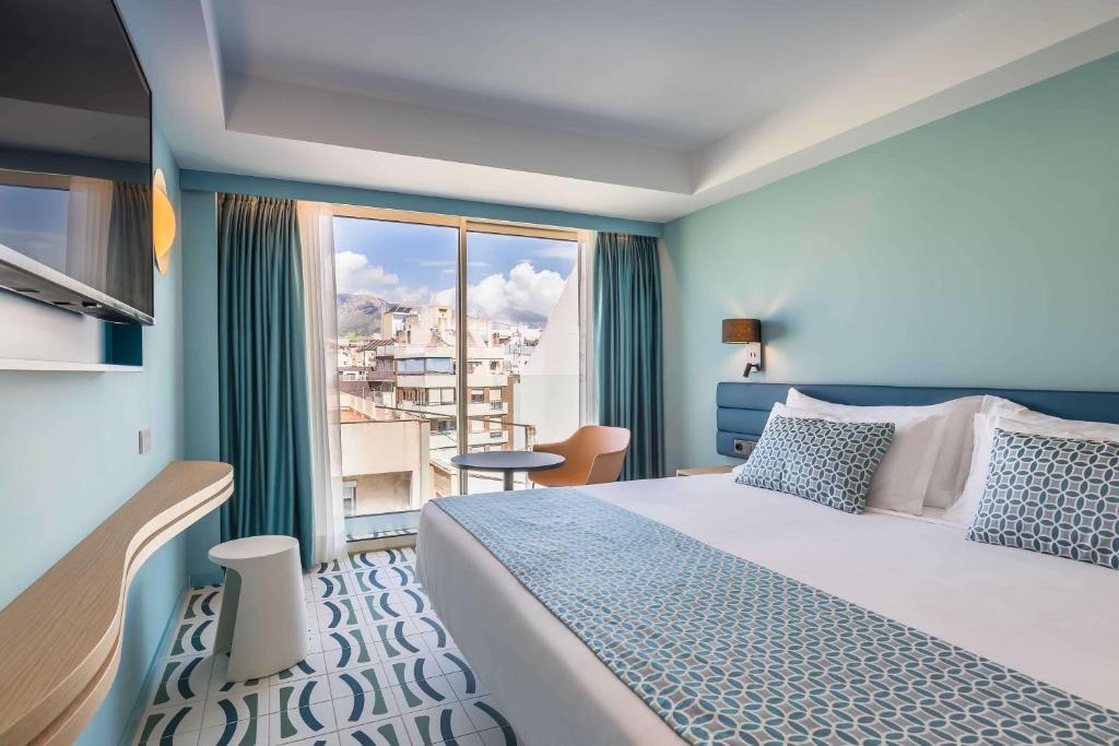 Mūsdienīga viesnīcas numura interjers ar skatu uz pilsētu, gaišām krāsām un stilīgu dizainu. Numurā ir liela gulta, televizors un neliels galds ar krēslu.