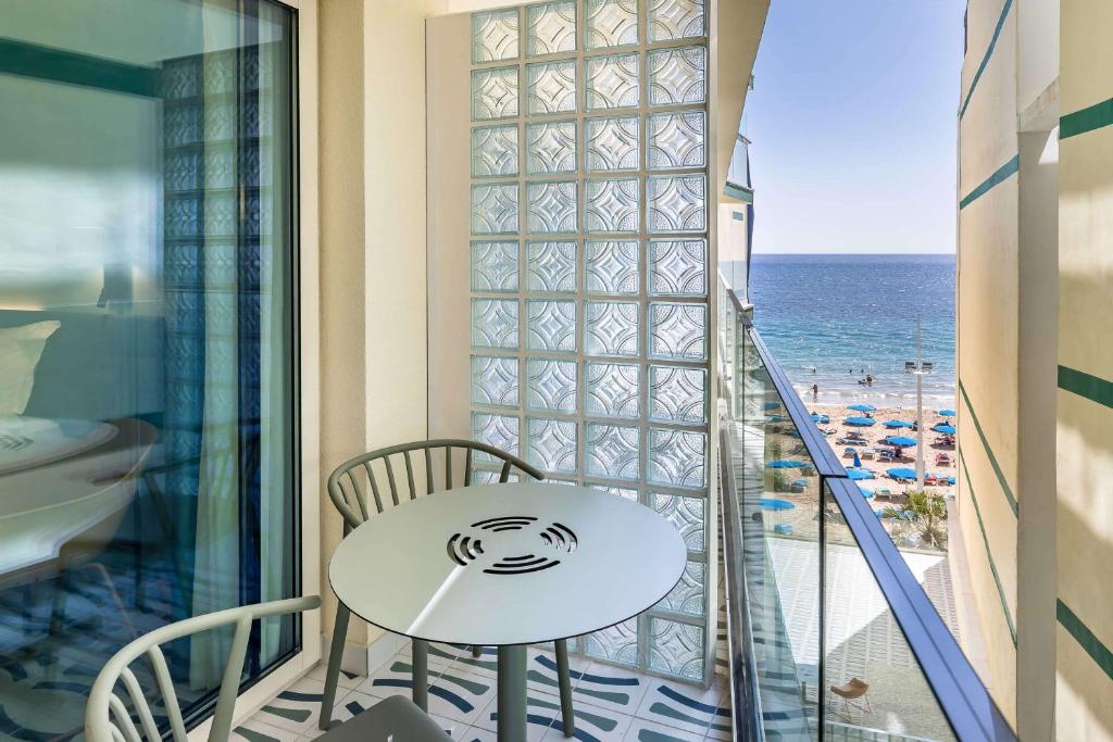 Balconā ar skatu uz jūru ir moderns galds un krēsli, kas nodrošina ērtu vietu relaksācijai. Jūras pludmales ainava ar sauļošanās krēsliem rada brīvdienu atmosfēru.