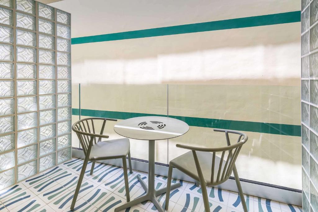 Mūsdienīgs interjers ar stikla blokiem, divām krēsliem un apaļu galdu, ideāls nelielai atpūtai vai darba stacijai. Kombinētas krāsas un raksti rada patīkamu atmosfēru.