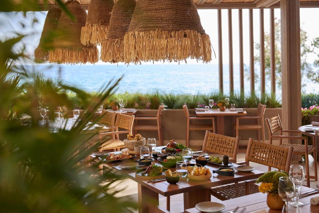 Elegants restorāns ar skatu uz jūru, kur galdos ir izsmalcināti ēdieni un ziedi, radot patīkamu atmosfēru relaksācijai un gastronomiskām baudām.