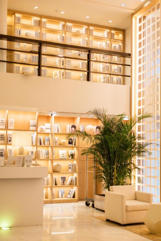 Mūsdienīga bibliotēka ar gaišiem plauktiem, kas piepildīti ar grāmatām, un ērtu sēdvietu, papildināta ar telpaugiem. Ideāli piemērota lasīšanai un relaksācijai.