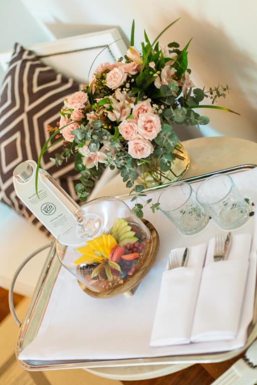 Skaisti ziedi un augļu plate uz galda, kopā ar glāzēm un galda piederumiem, radot viesmīlīgu atmosfēru.