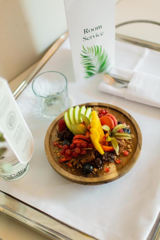 Svaigas augļu plate ar granolu un riekstiem, pasniegta uz koka šķīvja, kopā ar ūdens glāzi un numura apkalpošanas karti.