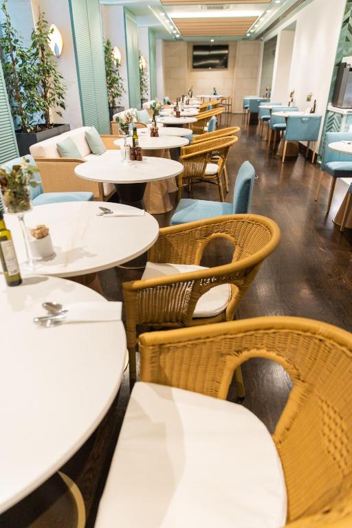 Klusā un eleganta restorāna interjers ar rīsu galdiem un komfortablām krēsliem, kas izveidots relaksējošai atmosfērai. Gaisma un zaļumi piešķir telpai svaigumu.