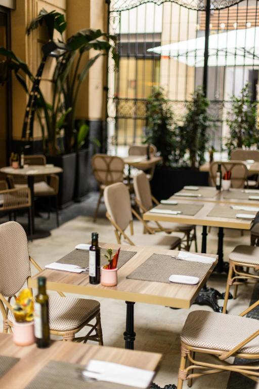 Mūsdienīgas restorāna iekštelpas ar elegantiem galdiem un krēsliem, kas aprīkoti ar zaļumiem un dekoratīviem elementiem. Gaisīga atmosfēra un harmonisks dizains.