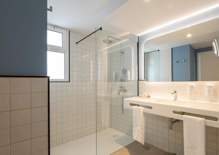 Mūsdienīgs vannas istabas interjers ar stikla dušas kabīni, gaišām flīzēm un minimālistisku izskatu. Izcila apgaismojuma sistēma un elegantas sanitārtehniskās iekārtas.
