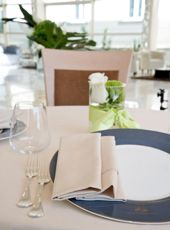 Eleganti iestatīts galds ar baltiem traukiem, sudraba galda piederumiem un ziedu kompozīciju. Galds ir dekorēts ar neitrālām krāsām un modernu dizainu.