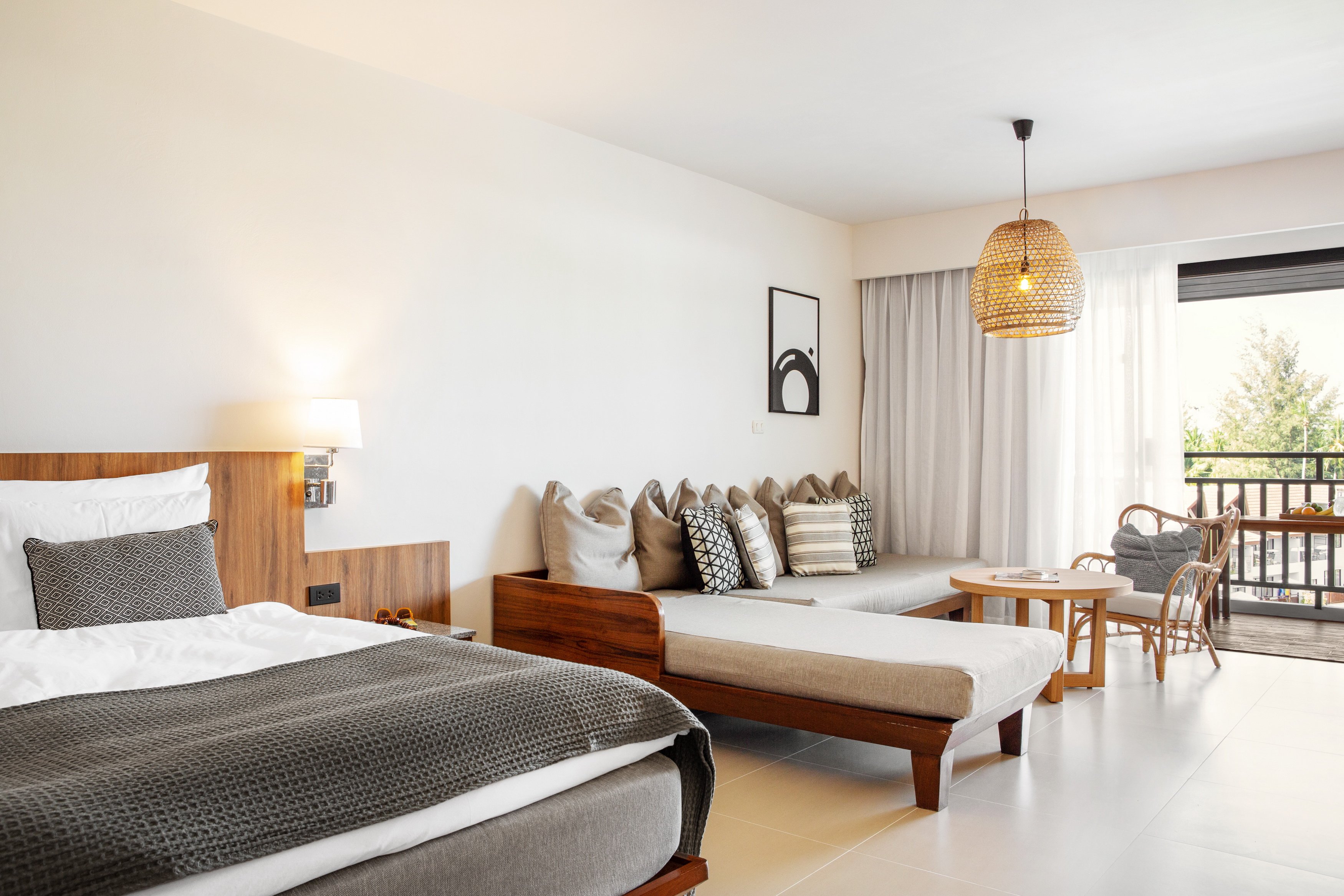 Sunwing Resort Kamala Beach moderns viesnīcas numurs ar lielu gultu, dīvānu, koka mēbelēm un balkonu ar skatu uz dārzu