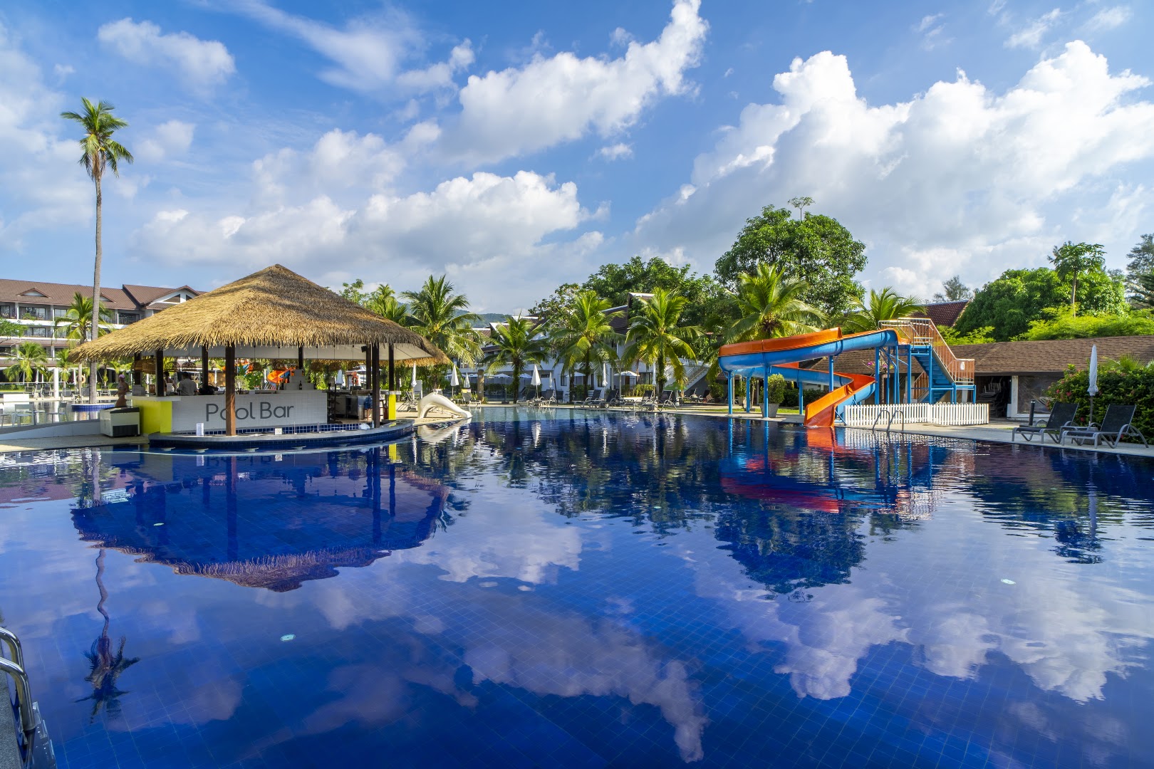 Sunwing Resort Kamala Beach plašais baseins ar centrālo bāru zem niedru jumta un ūdens slidkalniņu fonā Puketas piekrastē