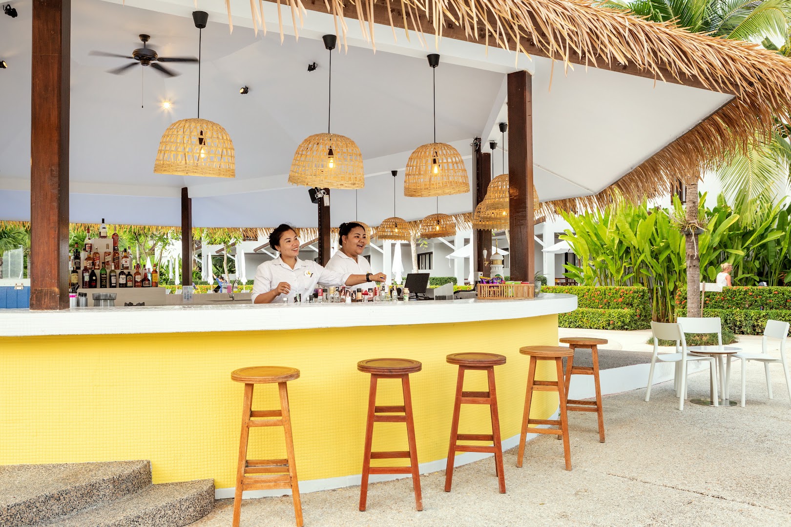 Sunwing Resort Kamala Beach baseina bārs ar dzeltenu apdari un darbiniekiem, kas gatavo dzērienus viesiem Puketas kūrortā