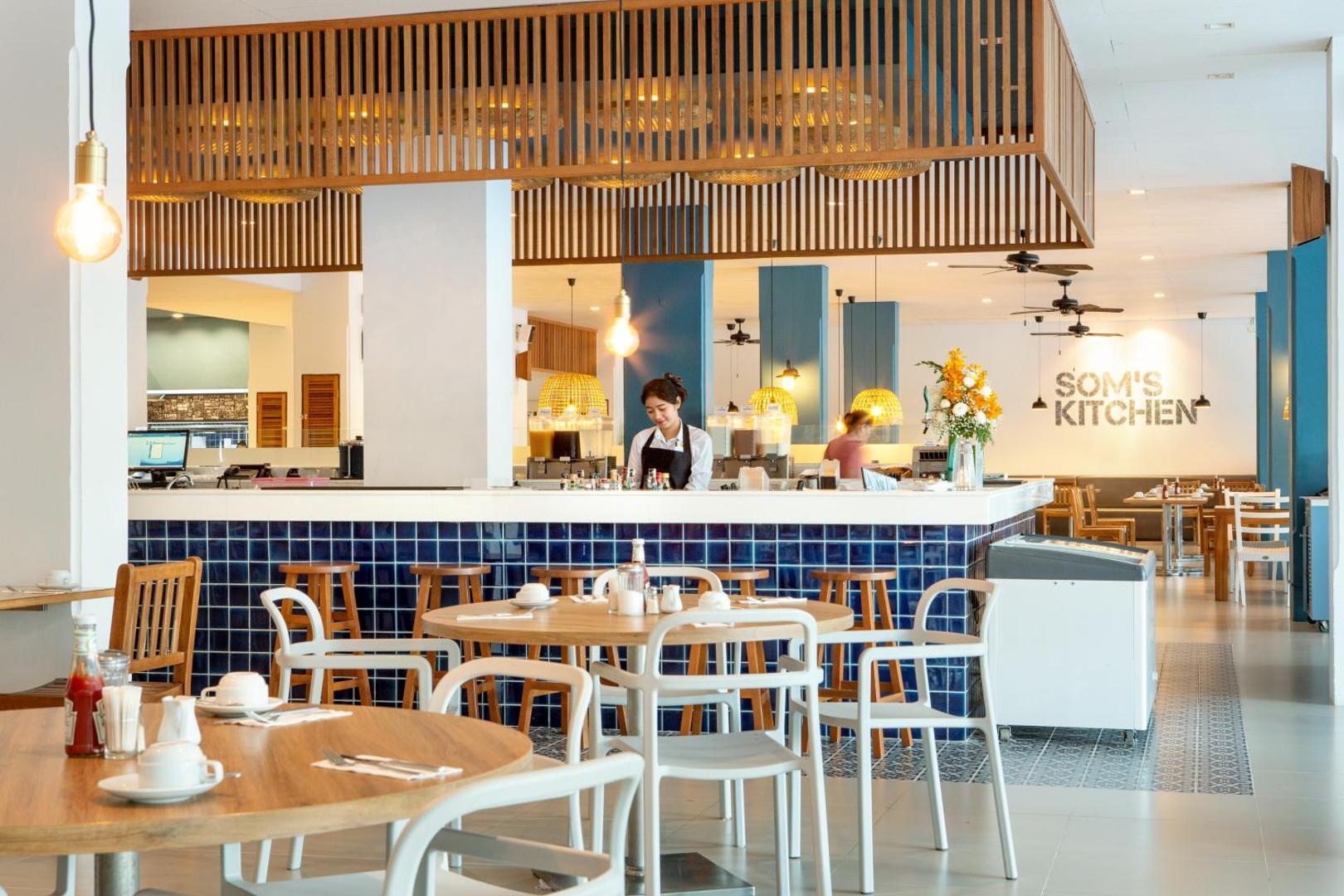 Sunwing Resort Kamala Beach restorāns Som's Kitchen ar zilu flīžu bāra leti, koka elementiem un viesmīlīgu personālu.