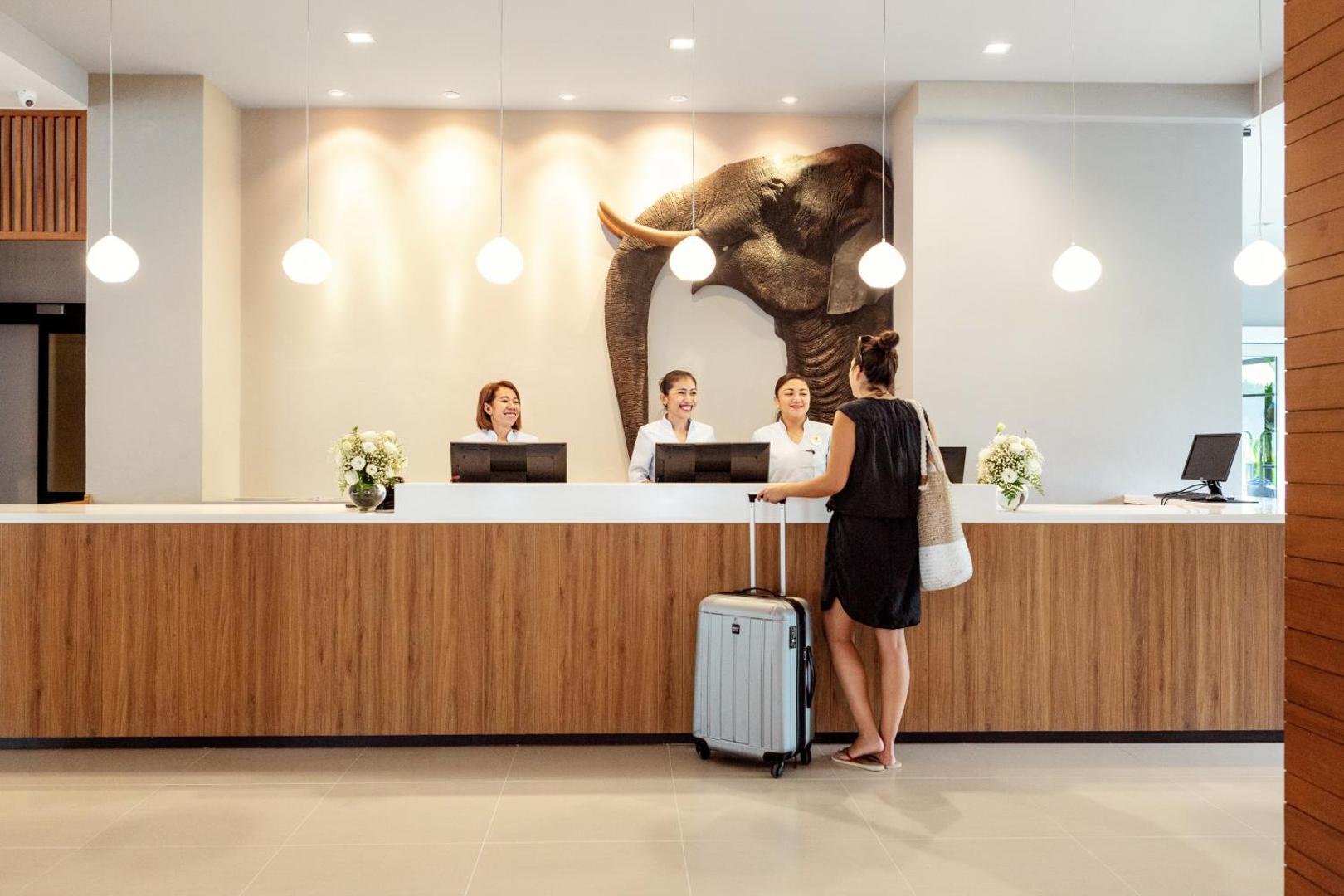 Sunwing Resort Kamala Beach recepcijas lete ar koka apdari, ziloņa galvas dekoru un smaidīgu personālu, kas apkalpo viesi.