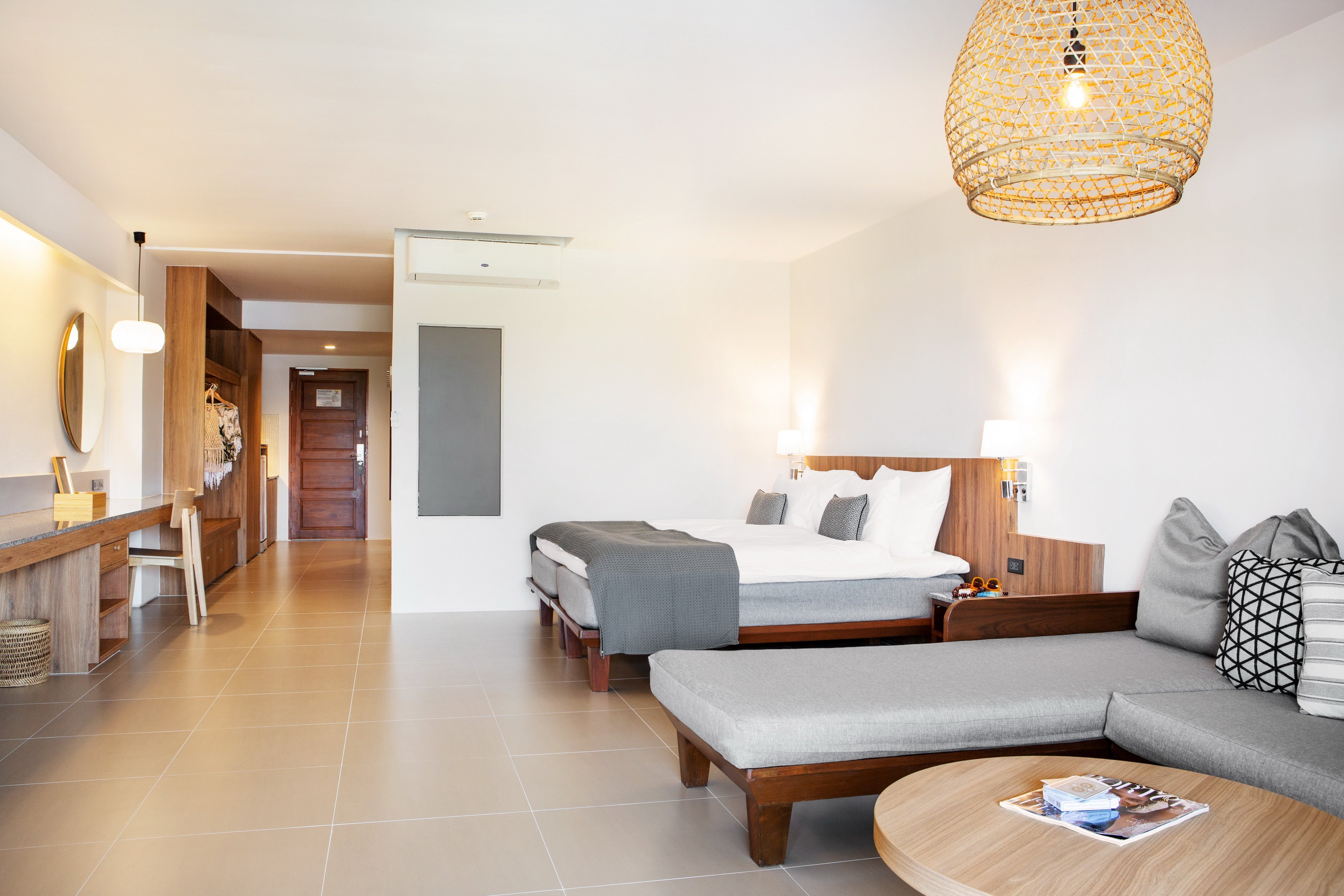 Sunwing Resort Kamala Beach viesnīcas numura interjers ar divguļamo gultu, stūra dīvānu, darba zonu un stilīgu pītu gaismekli