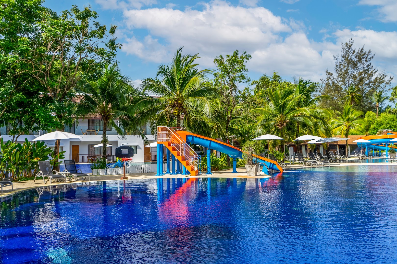 Sunwing Resort Kamala Beach āra baseins ar ūdens slidkalniņiem un palmu dārzu Puketā — atpūtas zona ar saulessargiem un zviļņiem