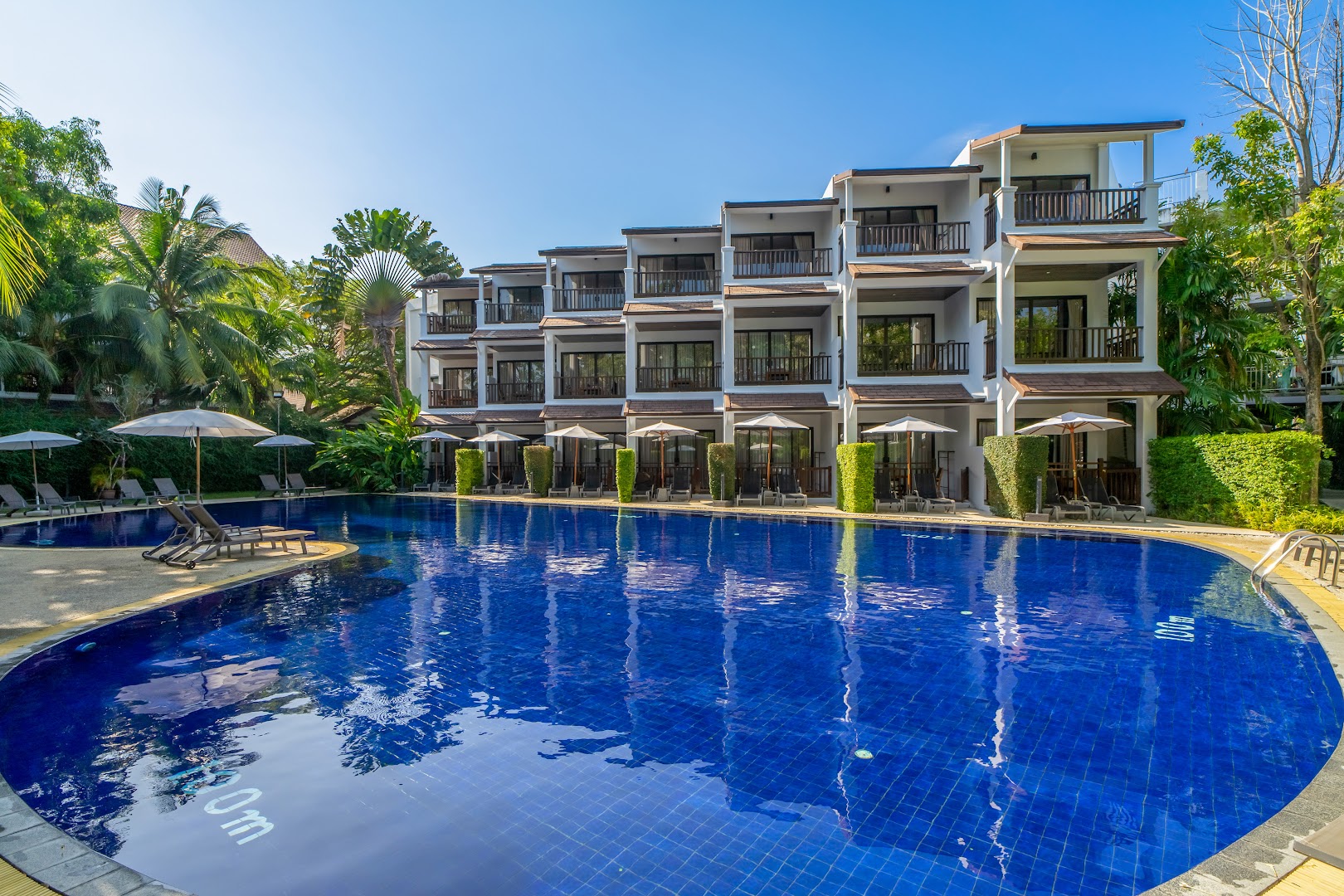 Sunwing Resort Kamala Beach āra baseins ar zilu flīžu apdari un saulessargiem pie viesnīcas korpusa ar balkoniem Puketā, Taizemē