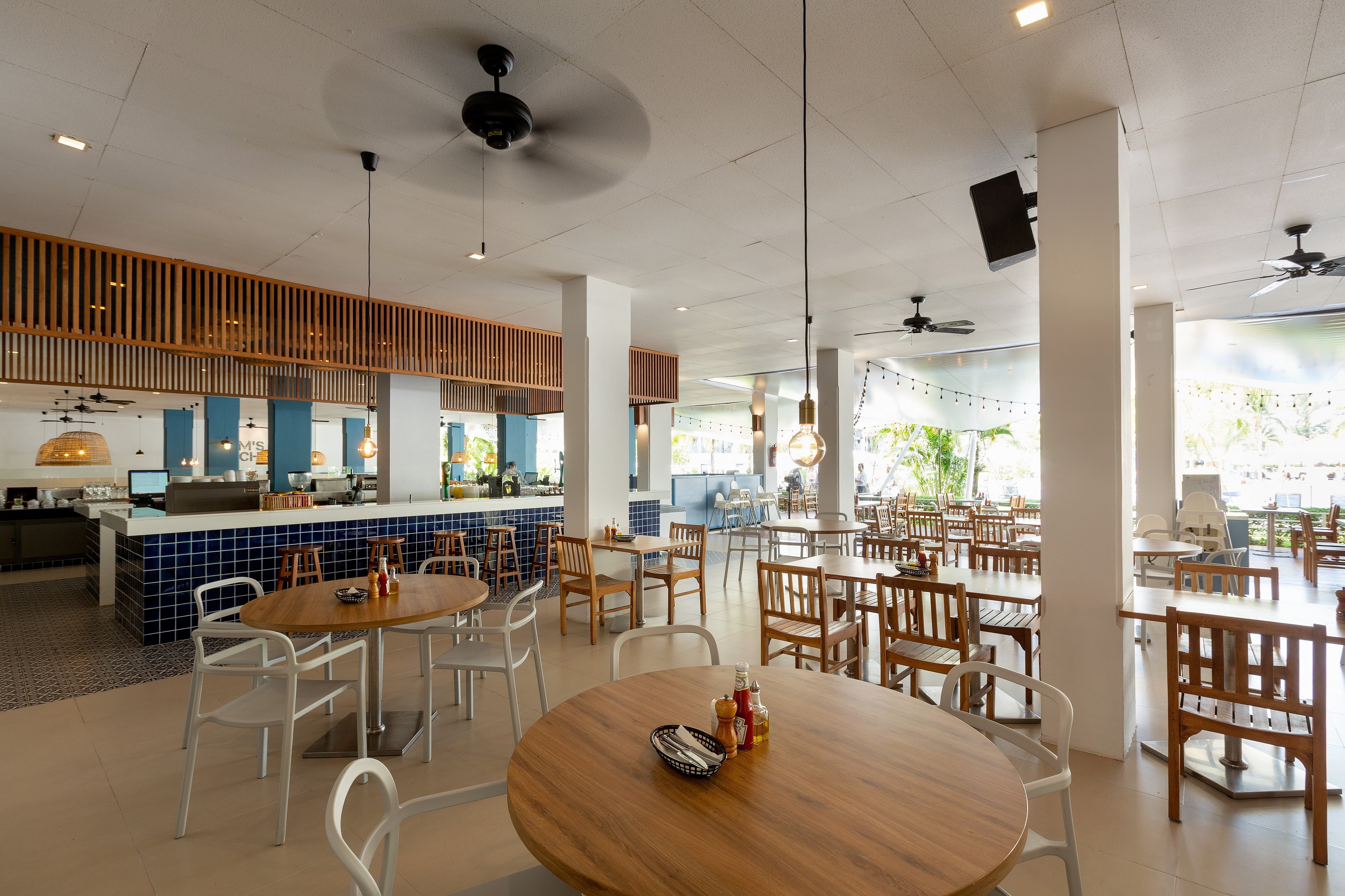 Sunwing Resort Kamala Beach bāra un restorāna zona ar koka galdiem, zilu flīžu apdari un atvērtu plānojumu uz terasi.