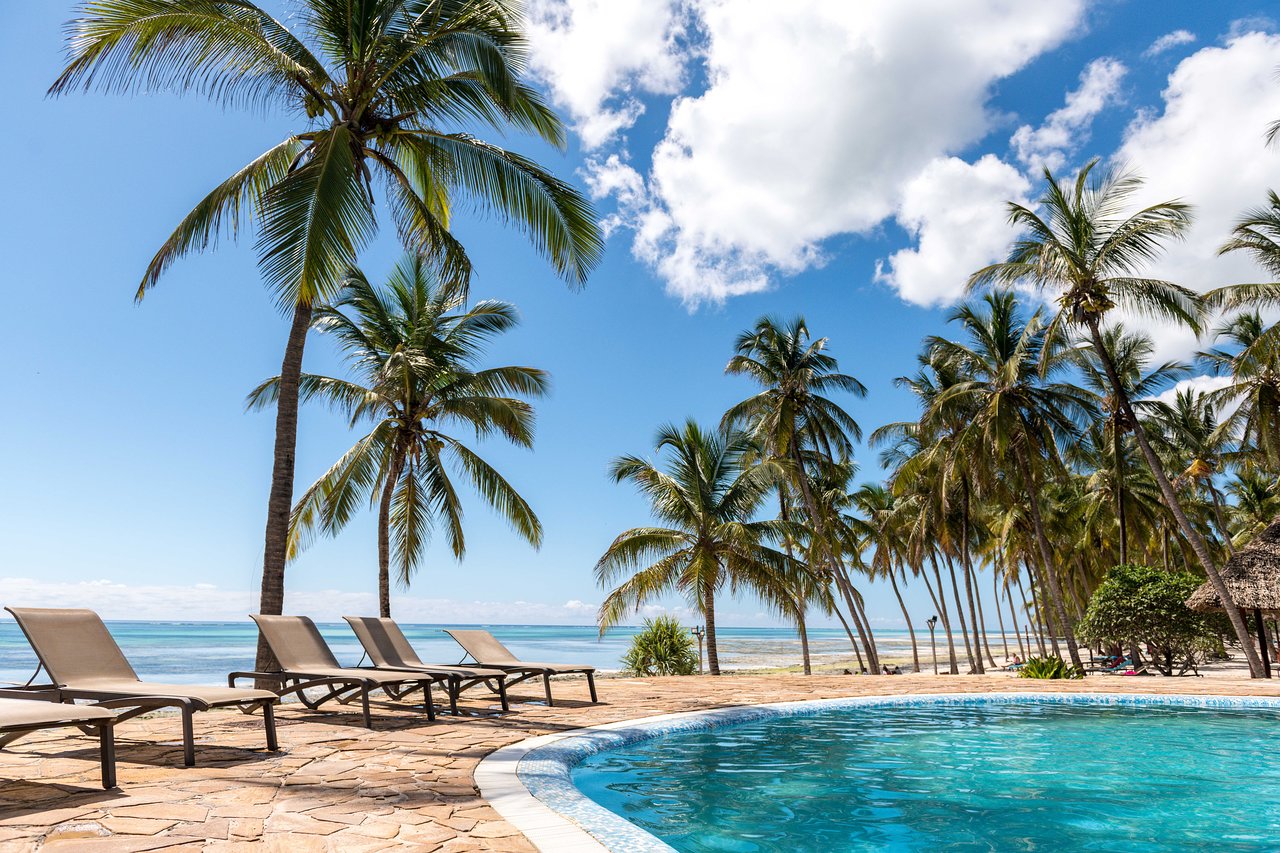 Tropu ainava ar palmām un peldbaseinu, kas atrodas pie pludmales, radot mierīgu un relaksējošu atmosfēru. Skaidrs debesis un zila jūra papildina šo idillisko skatu. panoramic view with beach and pools