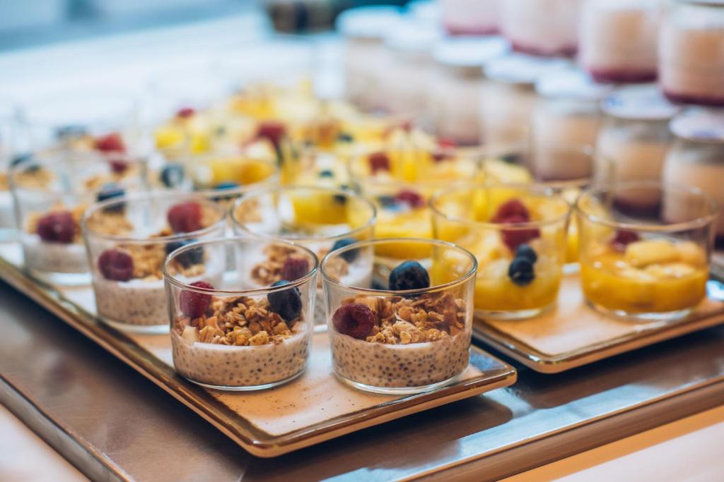 Svaigu augļu un granolas deserti glāzēs, kas novietoti uz plāksnes ar jogurta un augļu salātiem, rada pievilcīgu brokastu vai uzkodu variāciju.