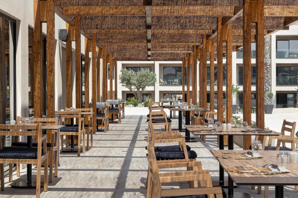 Vasaras terase Helea Lifestyle Beach Resort ar koka galdiem un krēsliem.