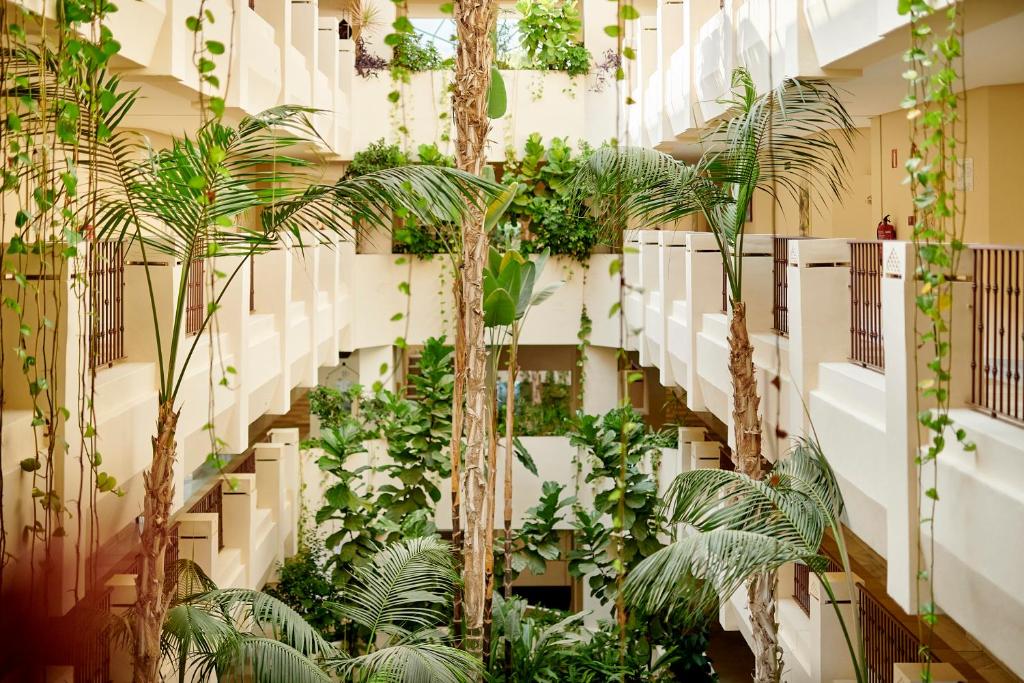 Zaļš iekšpagalms ar palmām un augiem, kas aug gar balkoniem, radot relaksējošu un dabīgu atmosfēru. Šis mūsdienu arhitektūras dizains ietver gaismas un augu harmoniju.