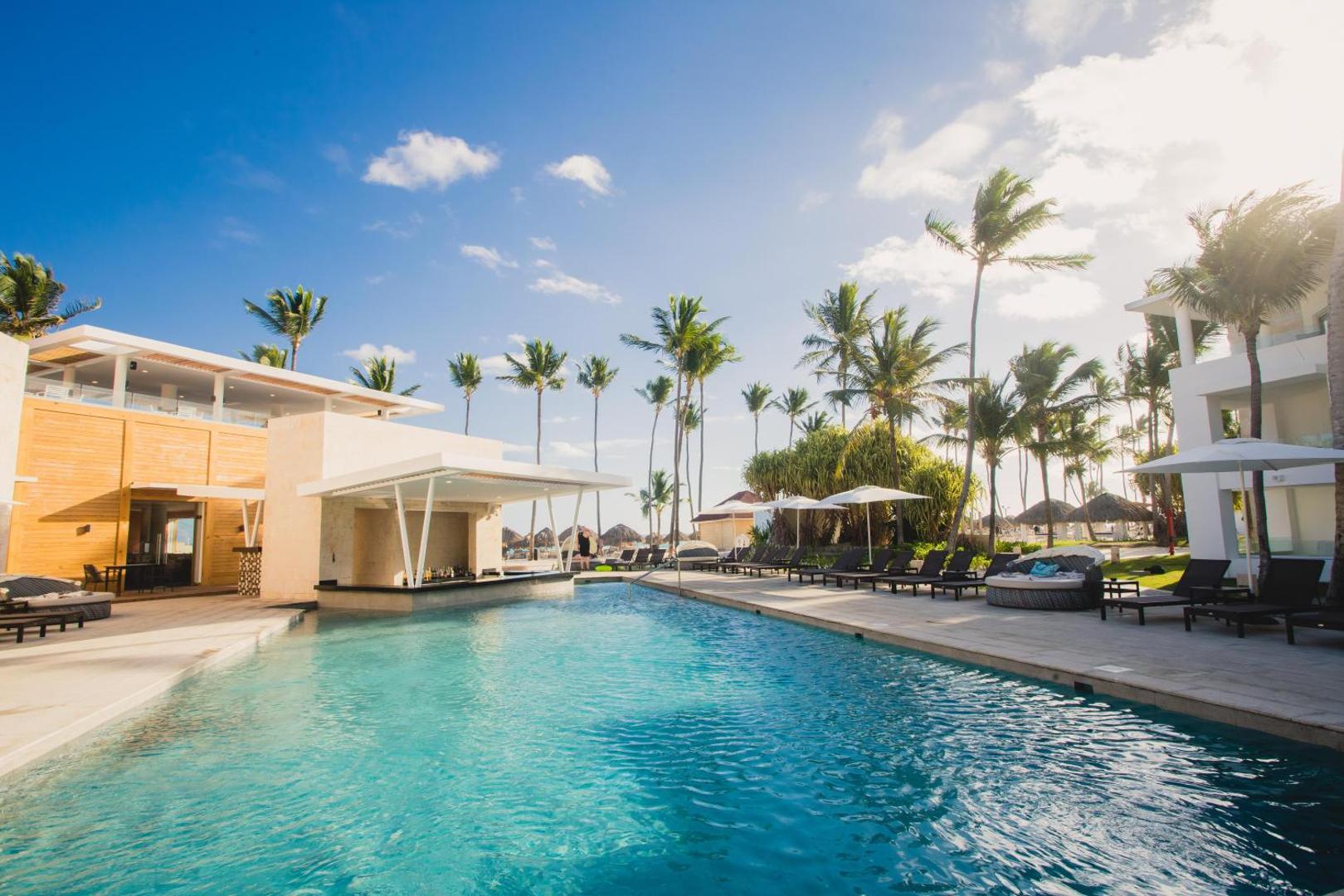 Grand Bavaro Princess baseina bārs un sauļošanās zona ar lietussargiem un ērtiem zviļņiem saulainā dienā