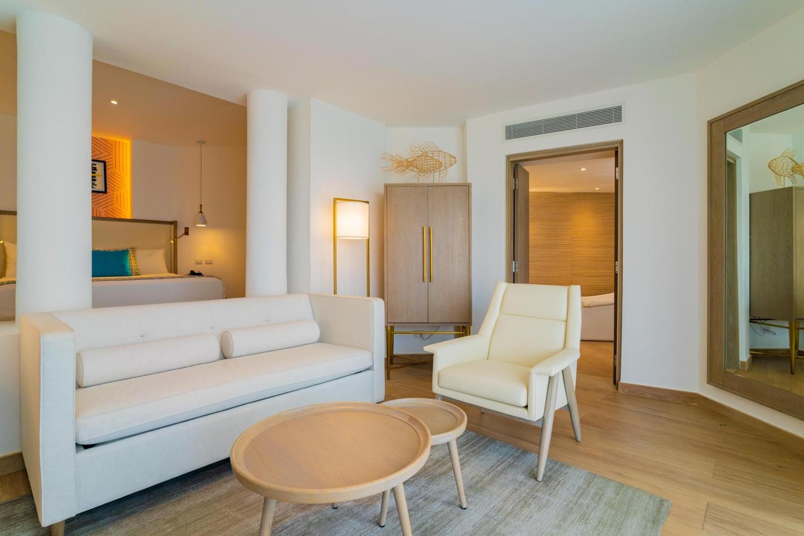 Grand Bavaro Princess suite numura dzīvojamā zona ar dīvānu, atpūtas krēslu un skatu uz guļamistabu