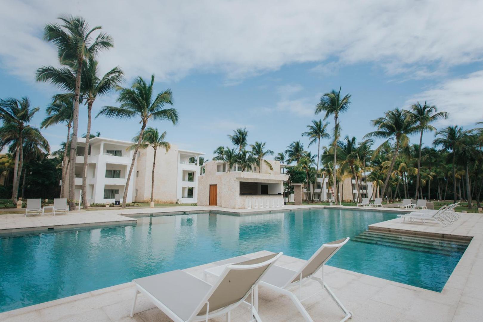 Grand Bavaro Princess kūrorta āra baseins ar gaišiem sauļošanās krēsliem un palmām Punta Kanā, Dominikānas Republikā