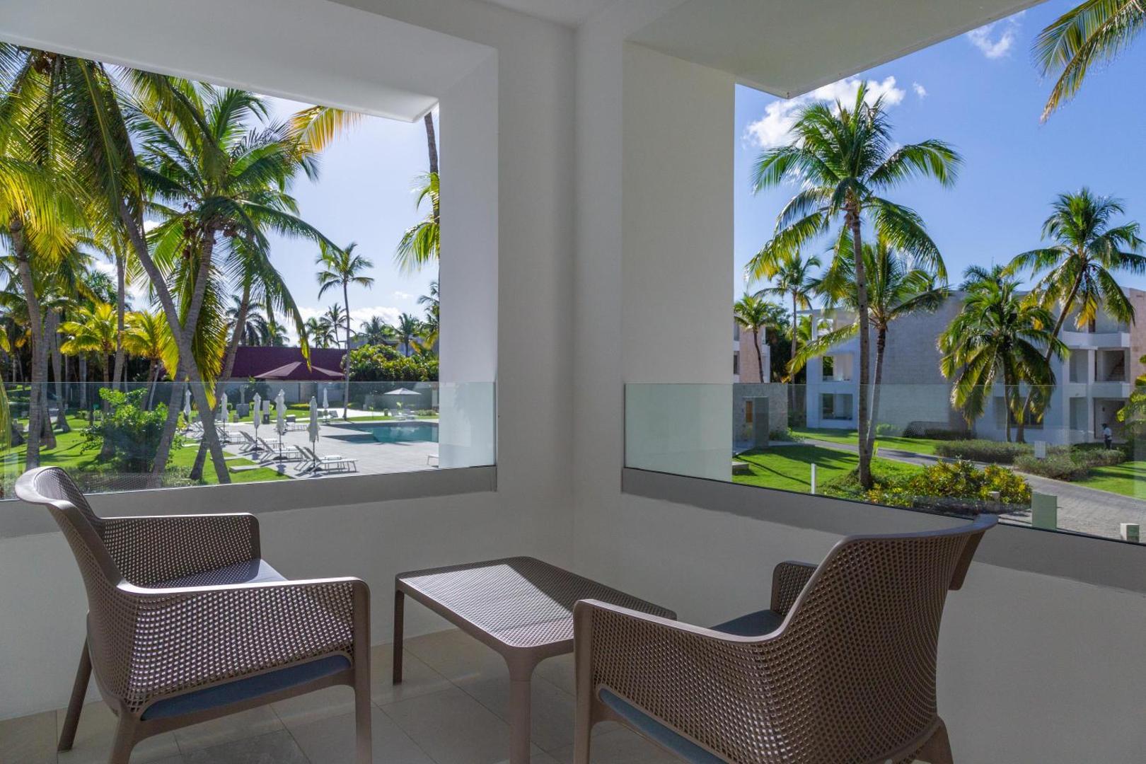 Grand Bavaro Princess numura balkons ar krēsliem un skatu uz viesnīcas dārzu, baseinu un palmām Punta Kanā, Dominikānā