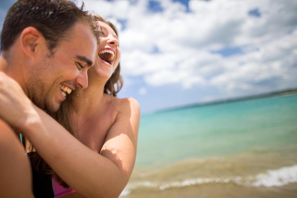 Jauna pāra laimīgas mirkļi pludmalē, izbaudot sauli un jūras viļņus. Viņu smaidi atspoguļo prieku un tuvību.